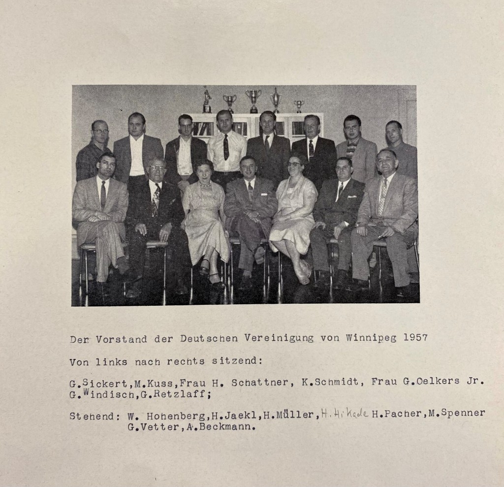 Photo of the board of the German Society of Winnipeg, 1957. Some members are seated, others are standing.