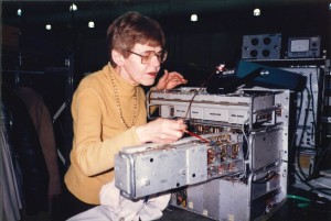 Photo of Elisabeth "Lisa" Schwabe at Lenkurt Electric (later Microtel, subsidiary of GTE), surrounded by technical machinery, taken in 1983.